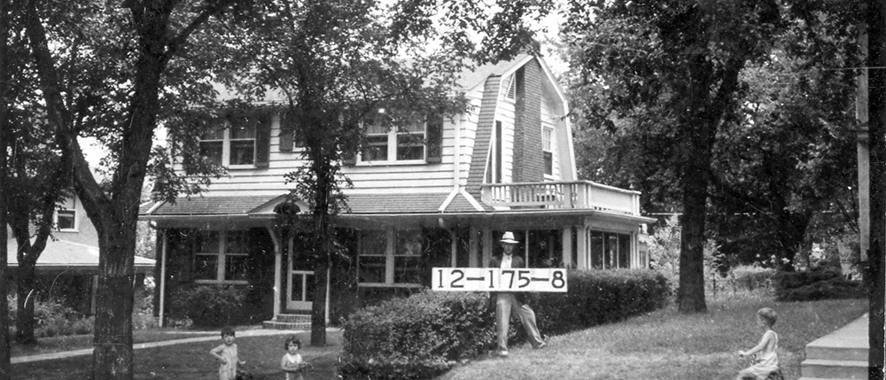 Photograph of a man holding a tax assessment placard in front of a home, flanked by two children