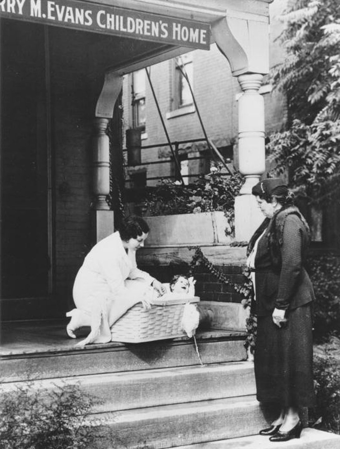 "Nurse with baby in basket on porch of K. C. Cradle. K.C., Mo.," circa 1930s