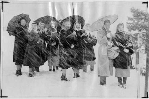 women holding umbrellas in a snowstorm at a bus stop