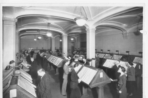 Library patrons reading newspapers on stands in a reading room