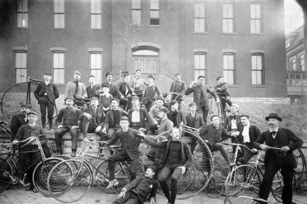 Black and white photograph of men posed on steps with bicycles