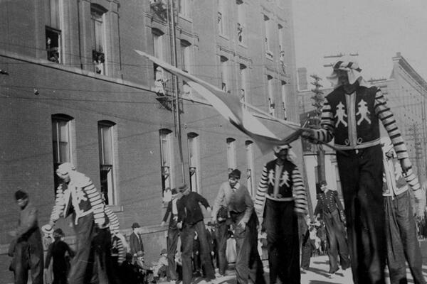 View of men on stilts in various dress walking along unidentified parade route during the Priests of Pallas parade.