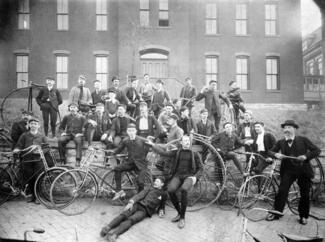 Black and white photograph of men posed on steps with bicycles